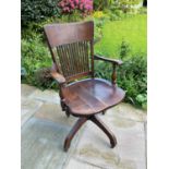 An Edwardian oak swivel office desk chair, with curved back and solid seat, on outswept legs with