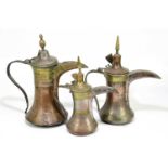 Three Persian copper and brass ewers, the tallest with iron handles, the smallest with a bronze