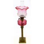 A late Victorian brass oil lamp with cranberry and clear glass shade, with wavy rim, etched with