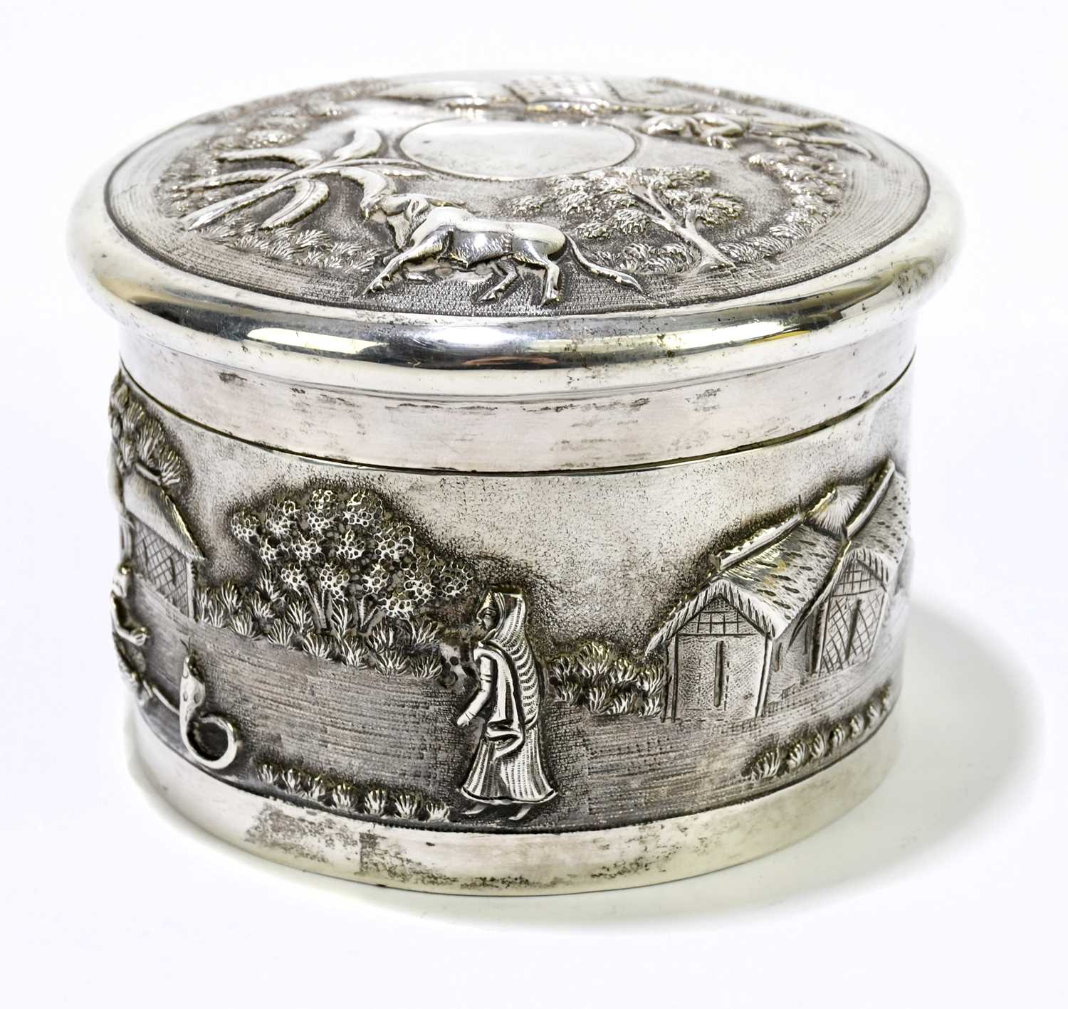 An Indian white metal lidded trinket box, decorated with village scenes.