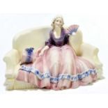 KATZHUTTE; a ceramic figure of a maiden with a fan and bonnet seated upon a sofa, impressed and