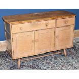 ERCOL; a mid century light elm sideboard with two drawers above three panelled cupboard doors on