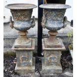 A pair of cast iron garden urns on stands, each twin handled urn on a square section stand with cast