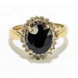 A 9ct yellow gold sapphire and diamond ring, the dark four claw set sapphire within a border of