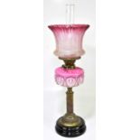 A Victorian oil lamp with cranberry and clear glass shade with etched floral decoration above the