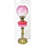 An early 20th century oil lamp, the cranberry and milk glass shade with etched floral decoration