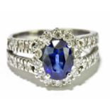 An 18ct white gold sapphire and diamond ring, the central oval four claw set sapphire within a