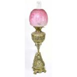 An unusual Victorian brass oil lamp with moulded cranberry glass shade above the Hanks & Son