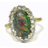 A yellow metal black opal and diamond set ring, the domed opal set within a border of twenty round