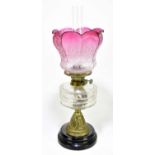 A Victorian oil lamp with cranberry and clear coloured shade, frosted decoration of floral sprays