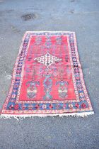 An Eastern style rug with central lozenge shaped motifs on a red ground. 220x132cm