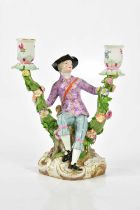 MEISSEN; a 19th century twin branch figural candle holder representing a seated male clutching the