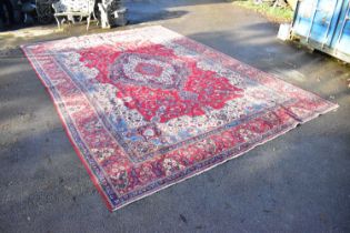 A large Eastern carpet decorated with stylised motifs and symbols on a predominantly red and blue