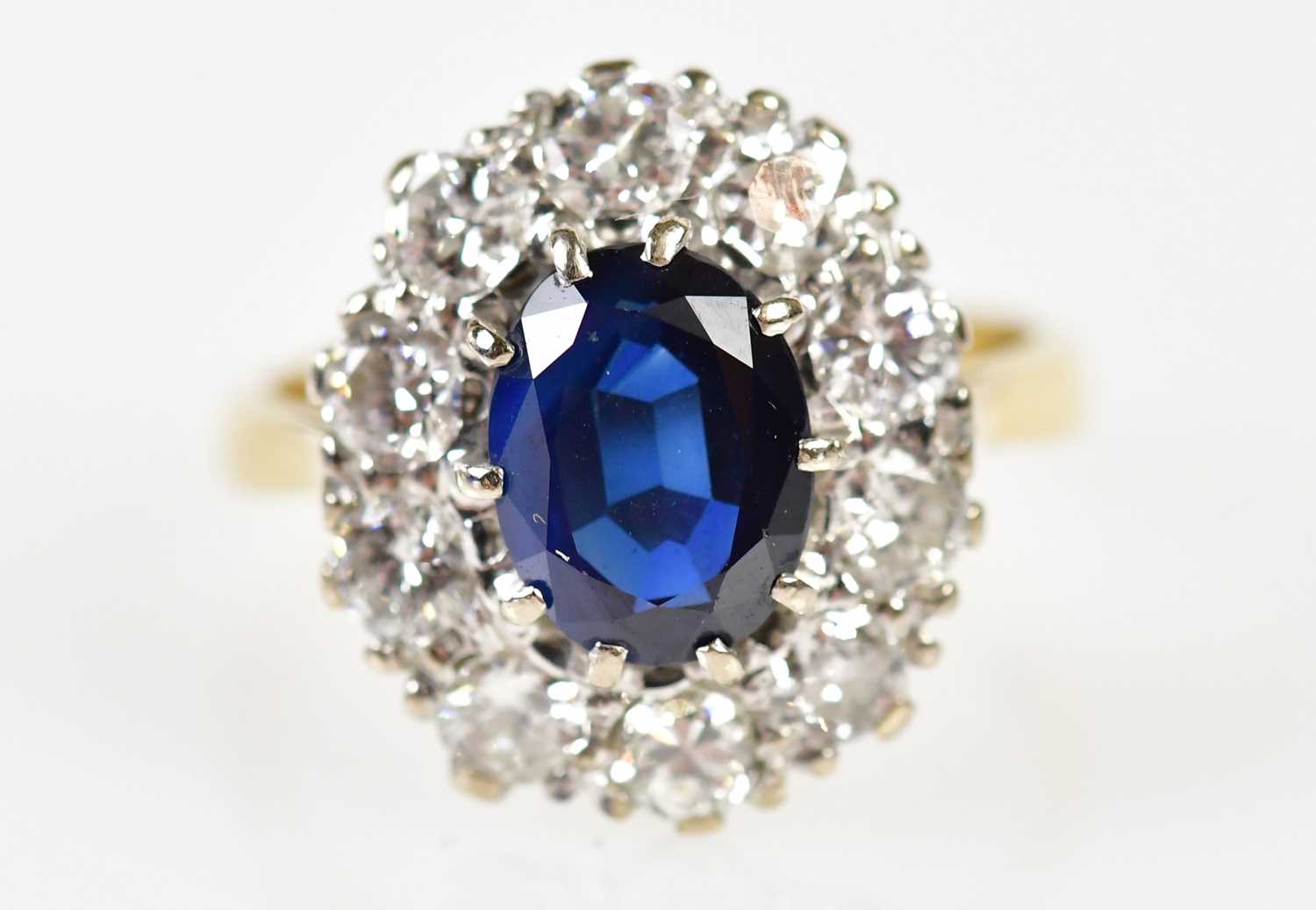 An 18ct yellow gold sapphire and diamond oval cluster ring, the claw set raised sapphire within a