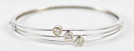 An 18ct white gold three stone diamond set hinged oval bangle, the three round brilliant cut