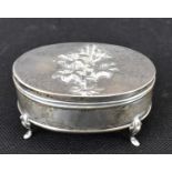 An Edwardian hallmarked silver oval lidded trinket box raised on four small feet, with embossed