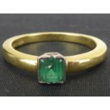 An 18ct gold emerald ring, the square set stepped emerald in a white love heart bezel mount, on an