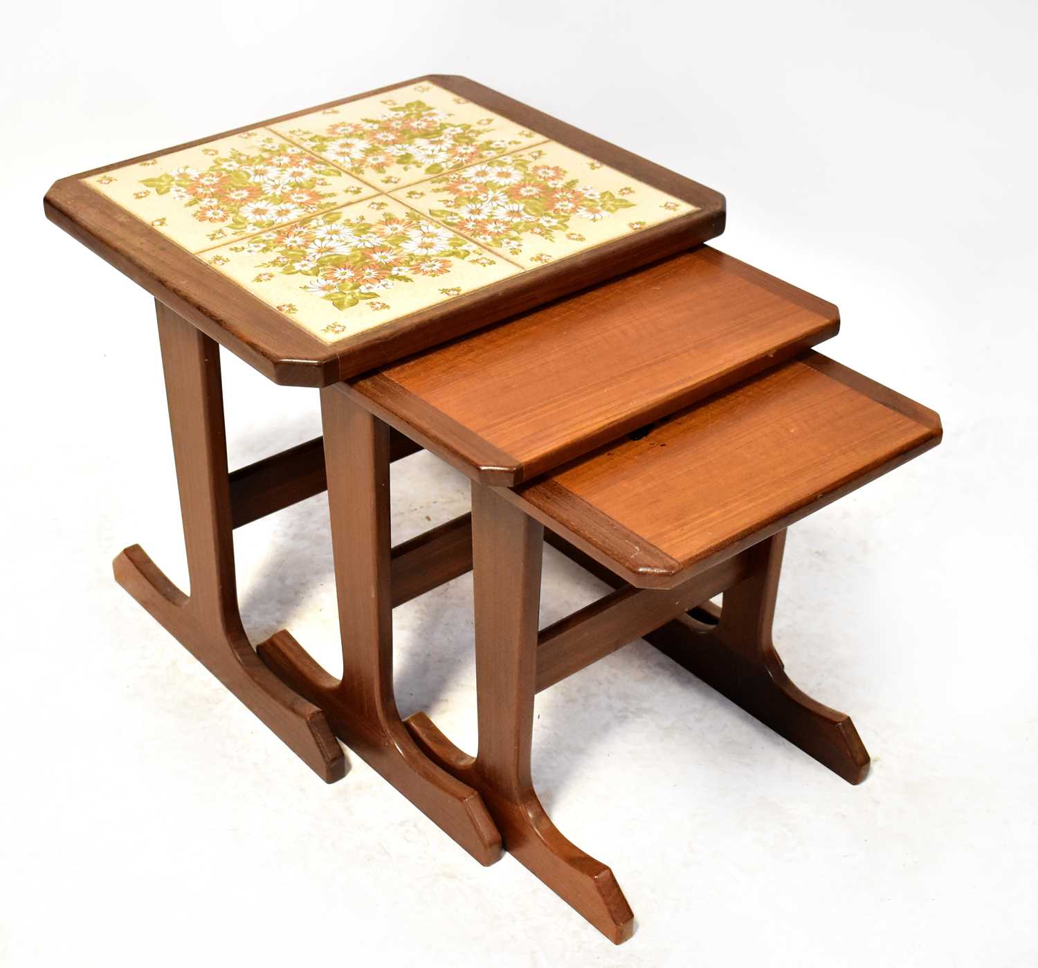 A retro dark stained teak nest of three tables, the largest set with four floral tiles, 45 x 49 x