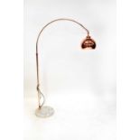 A modern standard lamp with a metal arched branch and domed shade, all in copper tones, on a