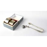 A pair of boxed hallmarked silver engine turned napkin rings, a pair of plated silver sugar tongs,