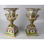 LUDWIGSBURG; a pair of 20th century porcelain twin-handled urns on square stands, each painted