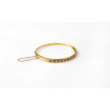 A 9ct gold bangle set with alternating rubies and diamonds, stamped 750, approx. 11.1g.