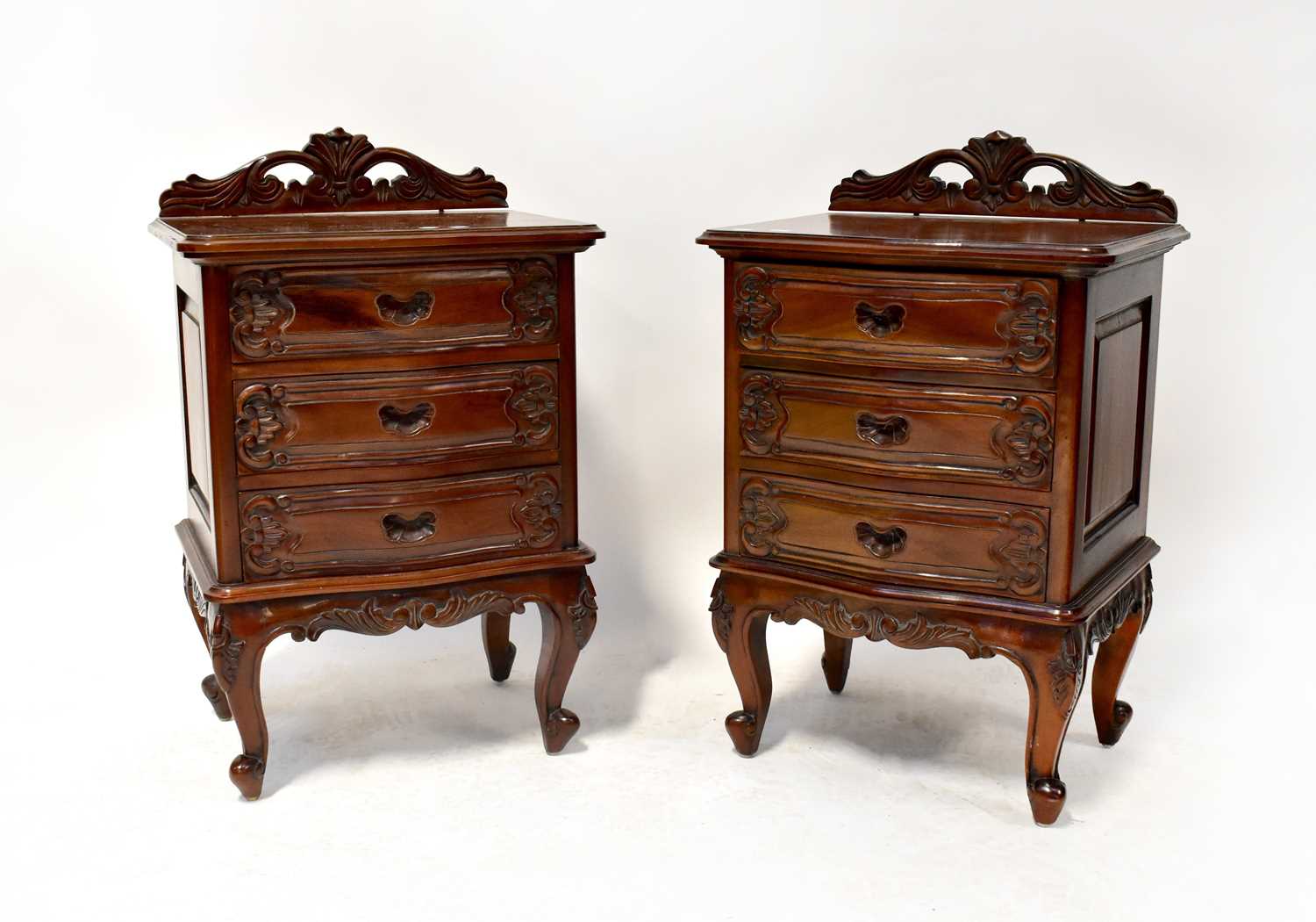 A pair of reproduction carved mahogany serpentine front three-drawer bedside cabinets with shaped