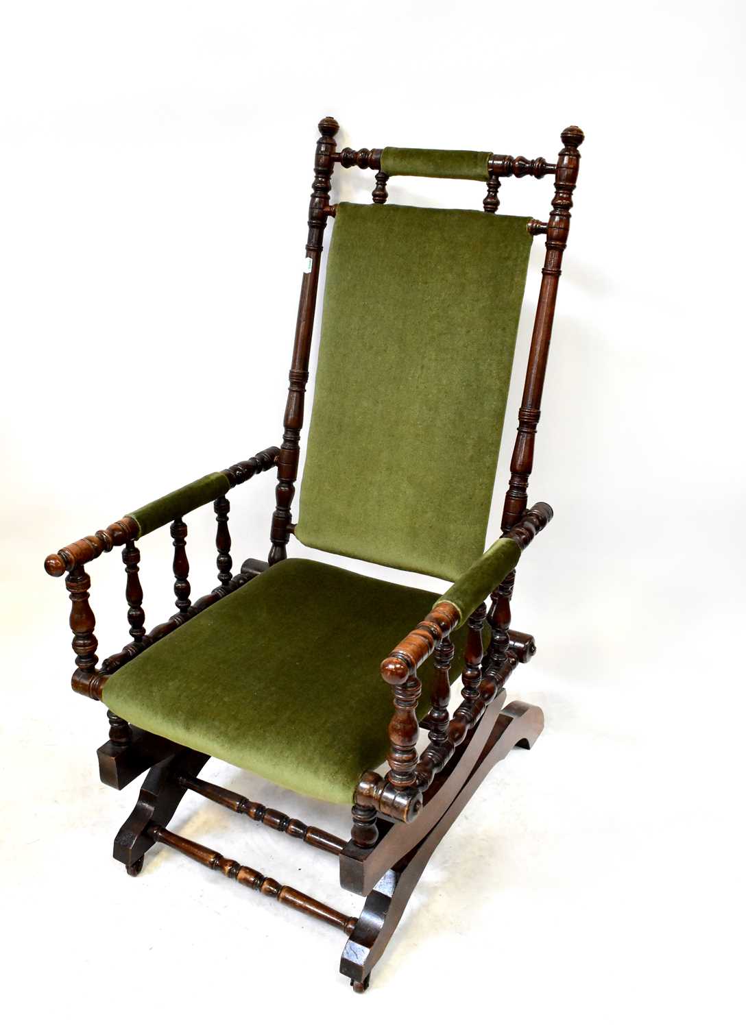 A walnut framed American rocking chair with turned supports and green velour upholstery.