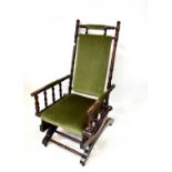 A walnut framed American rocking chair with turned supports and green velour upholstery.