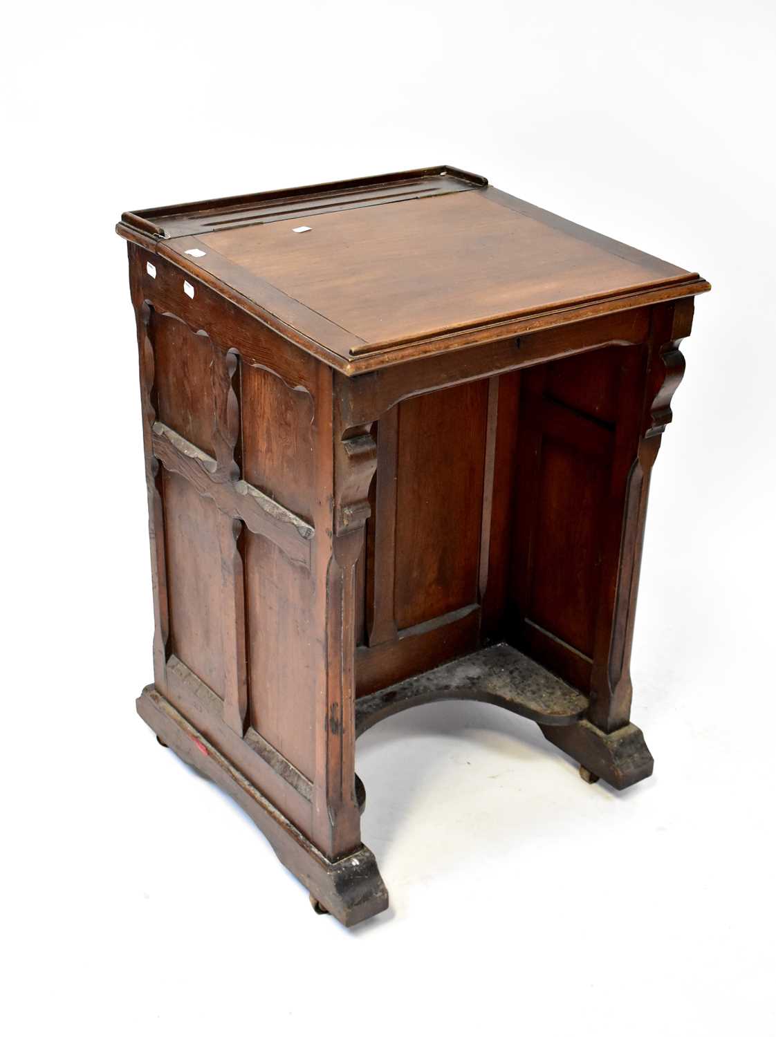 An Edwardian oak school desk with lift-up top, panelled sides and cupboard door to front, all to