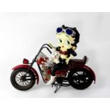 A large plaster and metal figure of 'Betty Boop' modelled sitting astride a motorbike with a puppy