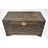 An early 20th century Oriental carved camphor wood chest with raised panel of figural and rural