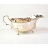 A George V hallmarked silver sauce boat with reeded border and scroll handle, raised on three paw