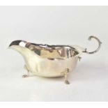 A George V hallmarked silver sauce boat with piecrust edge and flying scroll handle, raised on three