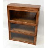 ANGUS; a mid-20th century three-tiered oak bookcase with glazed up-and-over doors, on a plinth base,