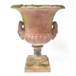 A contemporary reconstituted garden urn with figurehead handles, raised on a square section base,