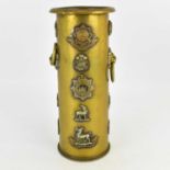 A Trench Art poker stand made from an artillery shell case, adorned with various military cap badges
