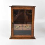 An early 20th century oak smokers' cabinet, the moulded top above single glazed door, fitted