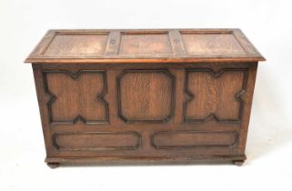 An early 20th century oak triple panelled coffer with carved detail to the lid, raised on squat