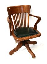 A 1920s mahogany revolving open arm office chair, with green leather studded base and slatted