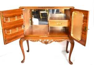 A reproduction walnut veneered cocktail cabinet with mirrored back and fitted interior, raised on