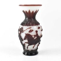 A Chinese Peking carved cameo glass vase in wine red and white, depicting riders and trees,