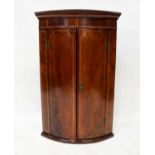 A mahogany line inlaid bow-fronted two-door wall-hanging corner cupboard with exposed brass