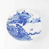 An Oriental blue and white plate painted with a landscape of pagoda amongst trees, with mountains in