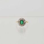 A yellow metal ring set with emerald cut green glass stone to centre, in a surround of fourteen