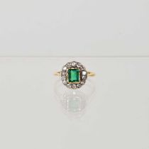 A yellow metal ring set with emerald cut green glass stone to centre, in a surround of fourteen