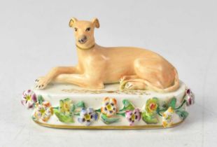 A 19th century Staffordshire model of a recumbent greyhound on a gilt and flower encrusted base,