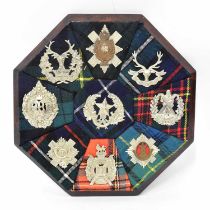 An octagonal oak plaque bearing the cap badges and tartans of all the Scottish regiments, diameter