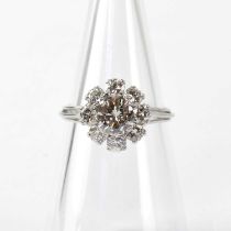 A white metal ring set with nine diamonds in a flower head formation, in claw settings and in a