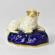 A Staffordshire model of a recumbent sheep on a blue painted rocky base, height 7.5cm, width 9cm.